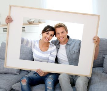 Cheerful-young-couple-holding-picture-frame-to-look-through