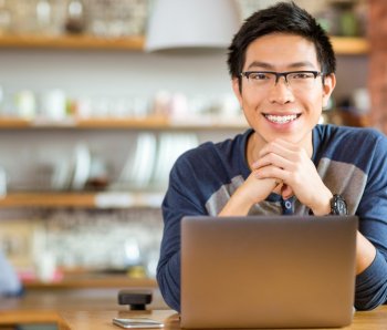 Portrait-of-positive-asian-male-in-glasses-with-laptop-in-cafe