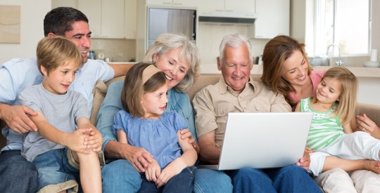 Smiling-multigeneration-family-using-laptop-in-living-room