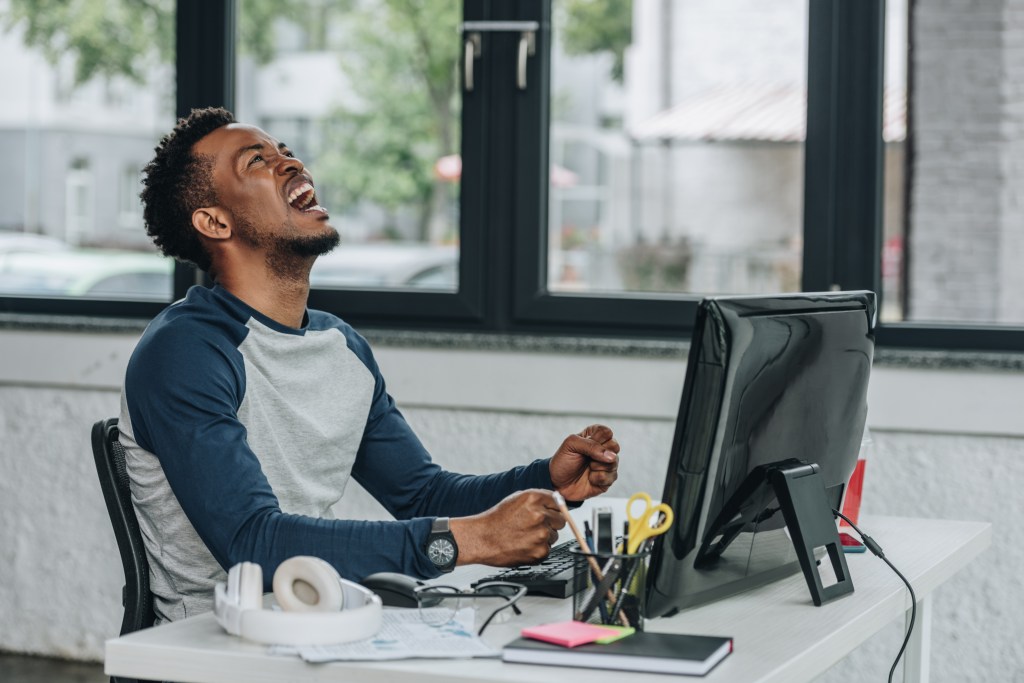 angry african american programmer gesturing while sitting at workplace in office