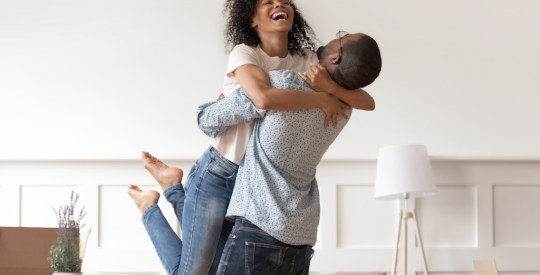 Husband lifting happy wife celebrating moving day with boxes
