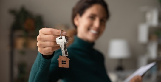 Close up focus on keys, smiling woman realtor selling apartment