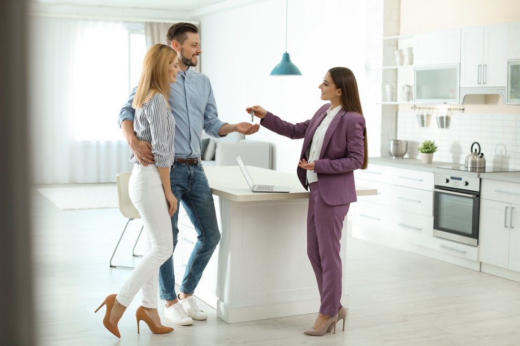 Female real estate agent giving house key to couple indoors